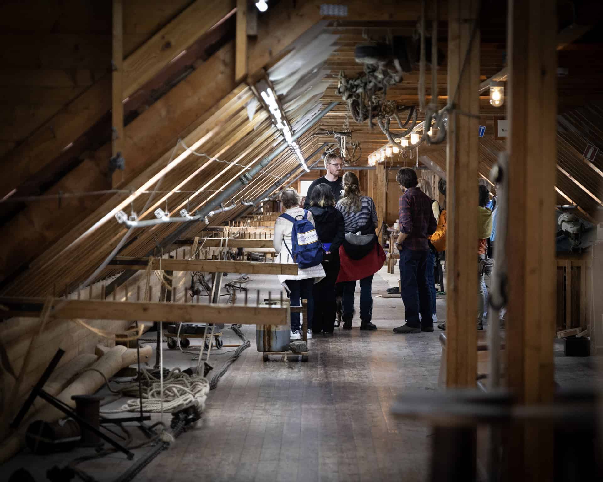 Båtbyggjar med hammar som arbeider med eit båtskrog som manglar flere plank