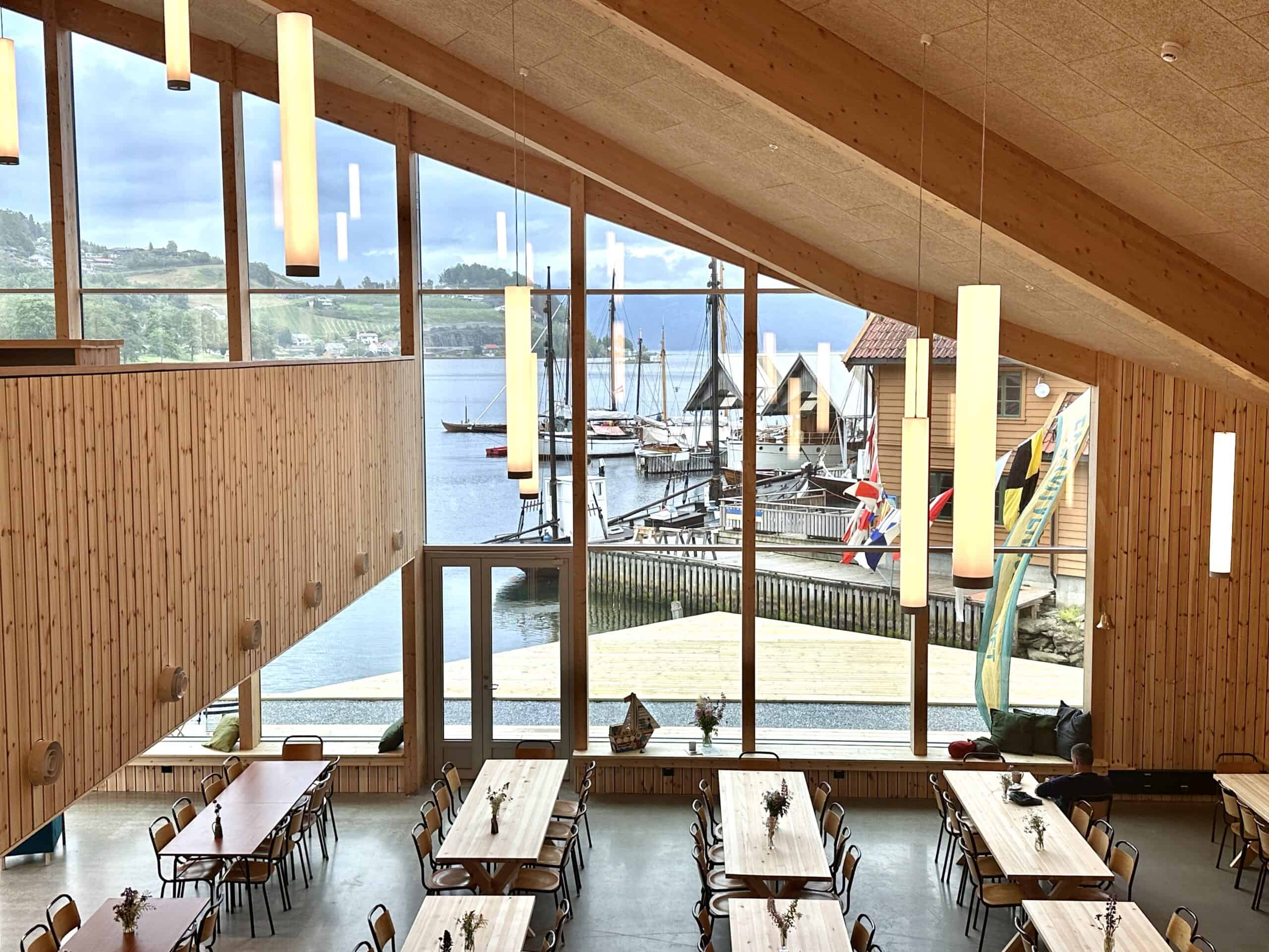 Overview of the café with many long tables. Large windows offer a view of boats and the sea.