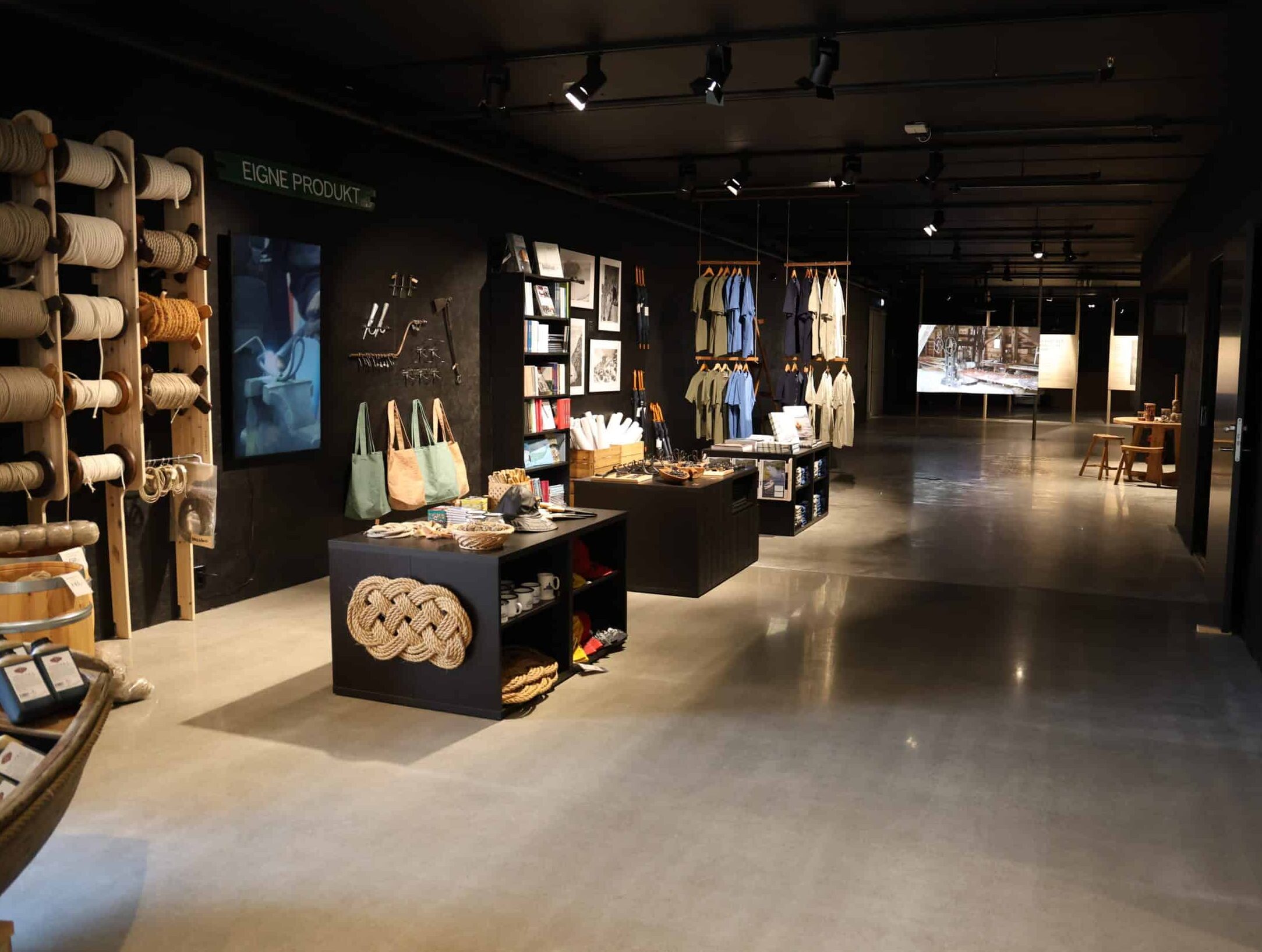 Museumsbutikk med flere bord med ulike produkter og bøker. to rekker med tau langs veggen.